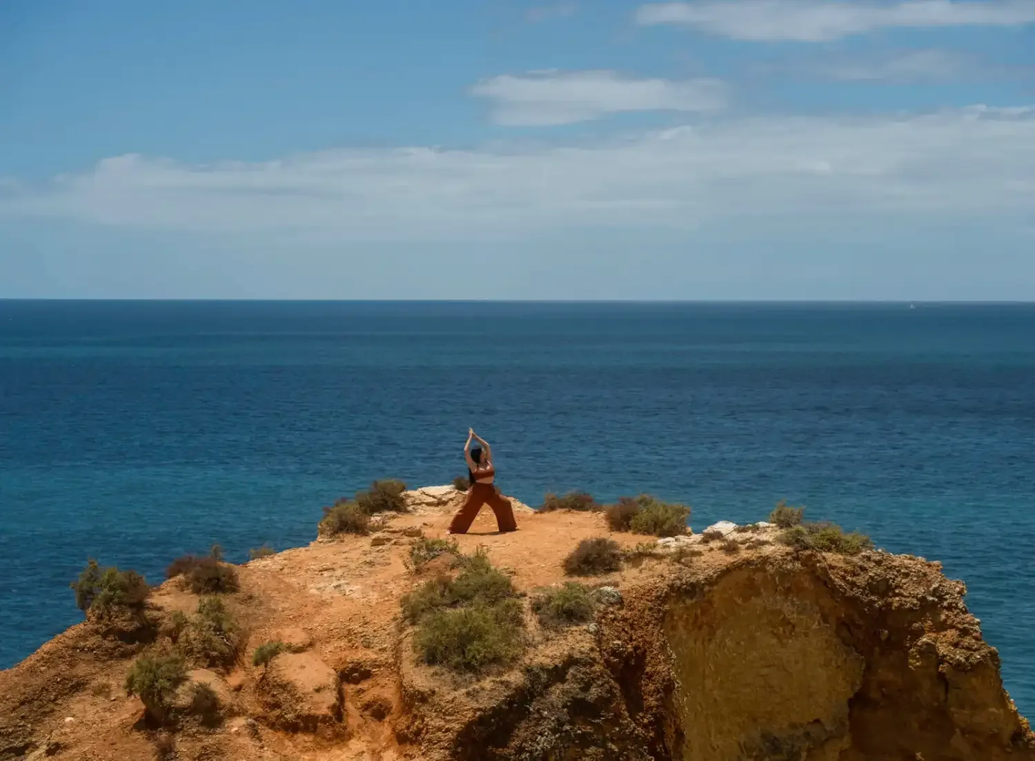 A figure seated in meditation on a red clifftop above the Atlantic